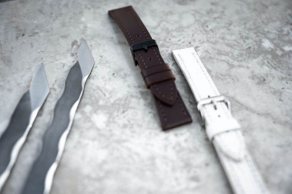 A pair of knives and a watch strap on a concrete surface.