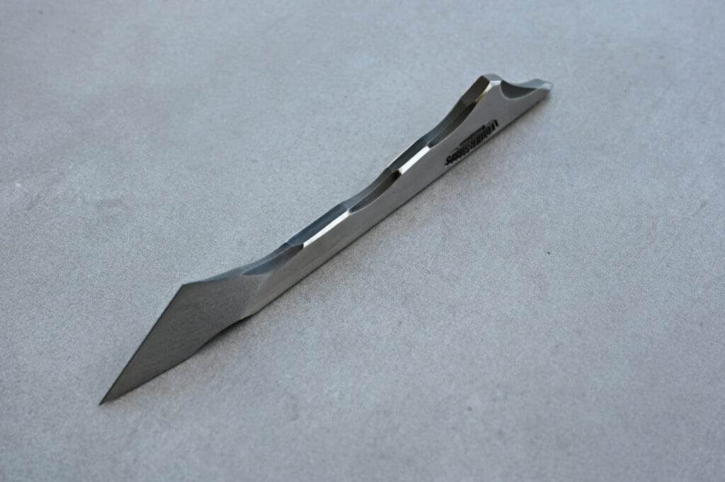 A metal blade scalpel resting on a concrete surface.