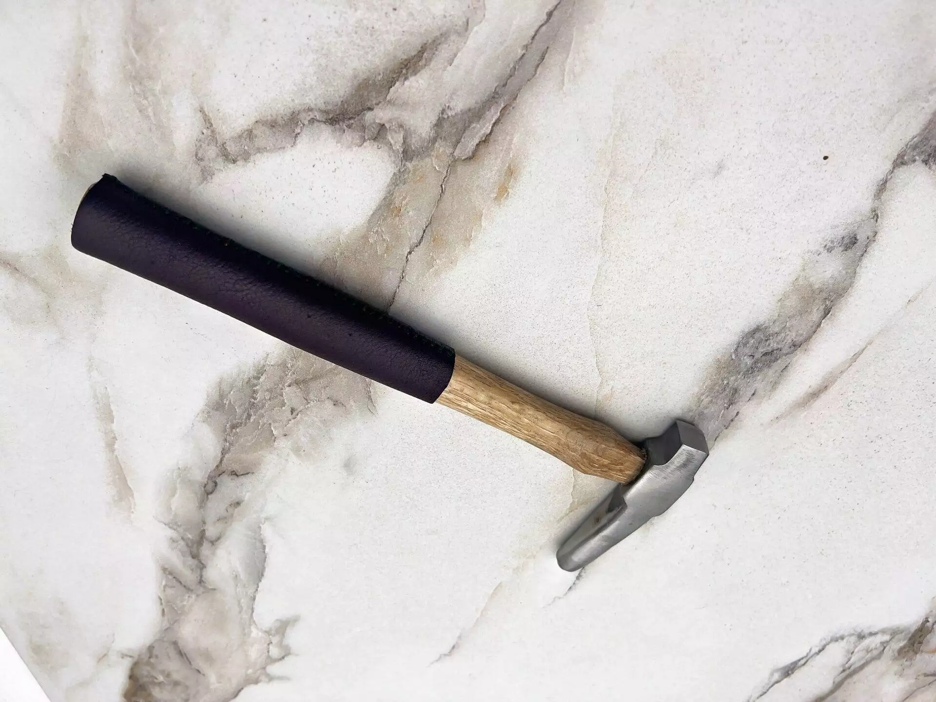 A Carbide Tipped Straightening Hammer with a wooden handle on a marble surface. (carbide, hammer)