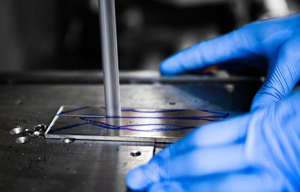 A person in blue gloves is working on a piece of metal wearing gloves.