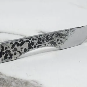 The Scorpion Skiver (45 Degree Bevel) with its speckled black and gray handle rests on a white and gray marbled surface.