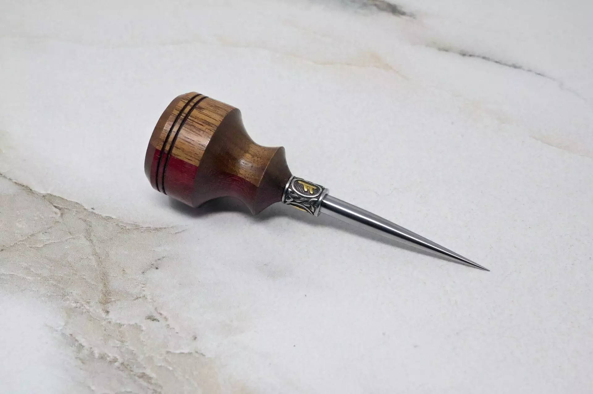 A small wooden tool on a marble surface, perfect for Christmas Special crafts requiring the 3 Piece Christmas Special - Small Awl, Essential Skiver and Riptide Scalpel.