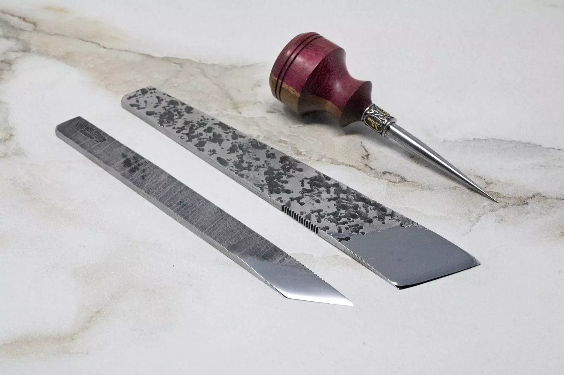 A pair of scissors and a knife, along with a 3 Piece Christmas Special - Small Awl, Essential Skiver and Riptide Scalpel, are displayed on a marble table.