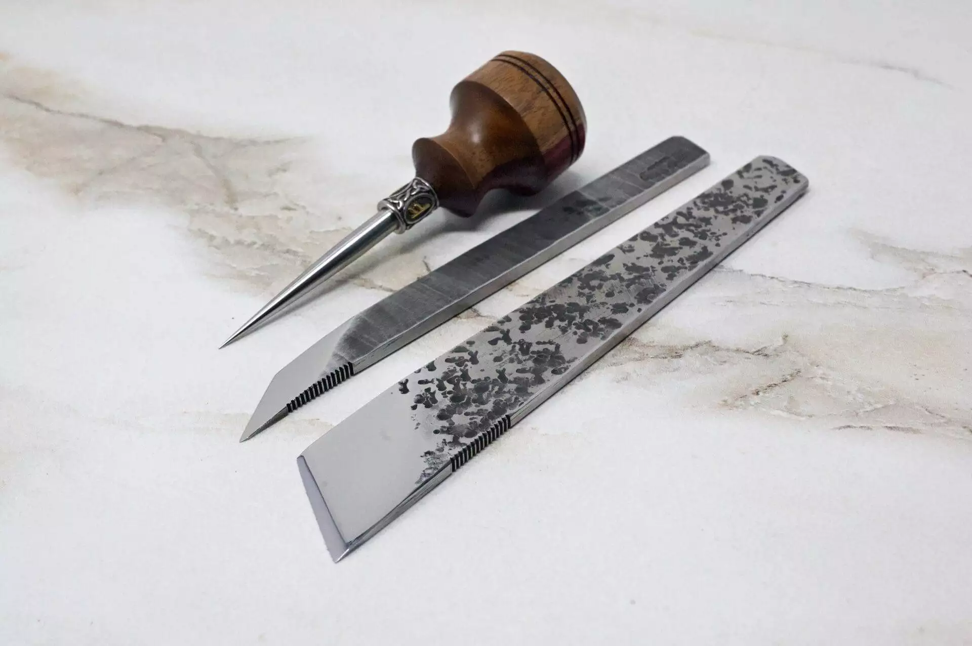 A pair of scissors, a knife, and a 3 Piece Christmas Special - Small Awl, Essential Skiver and Riptide Scalpel on top of a marble table.