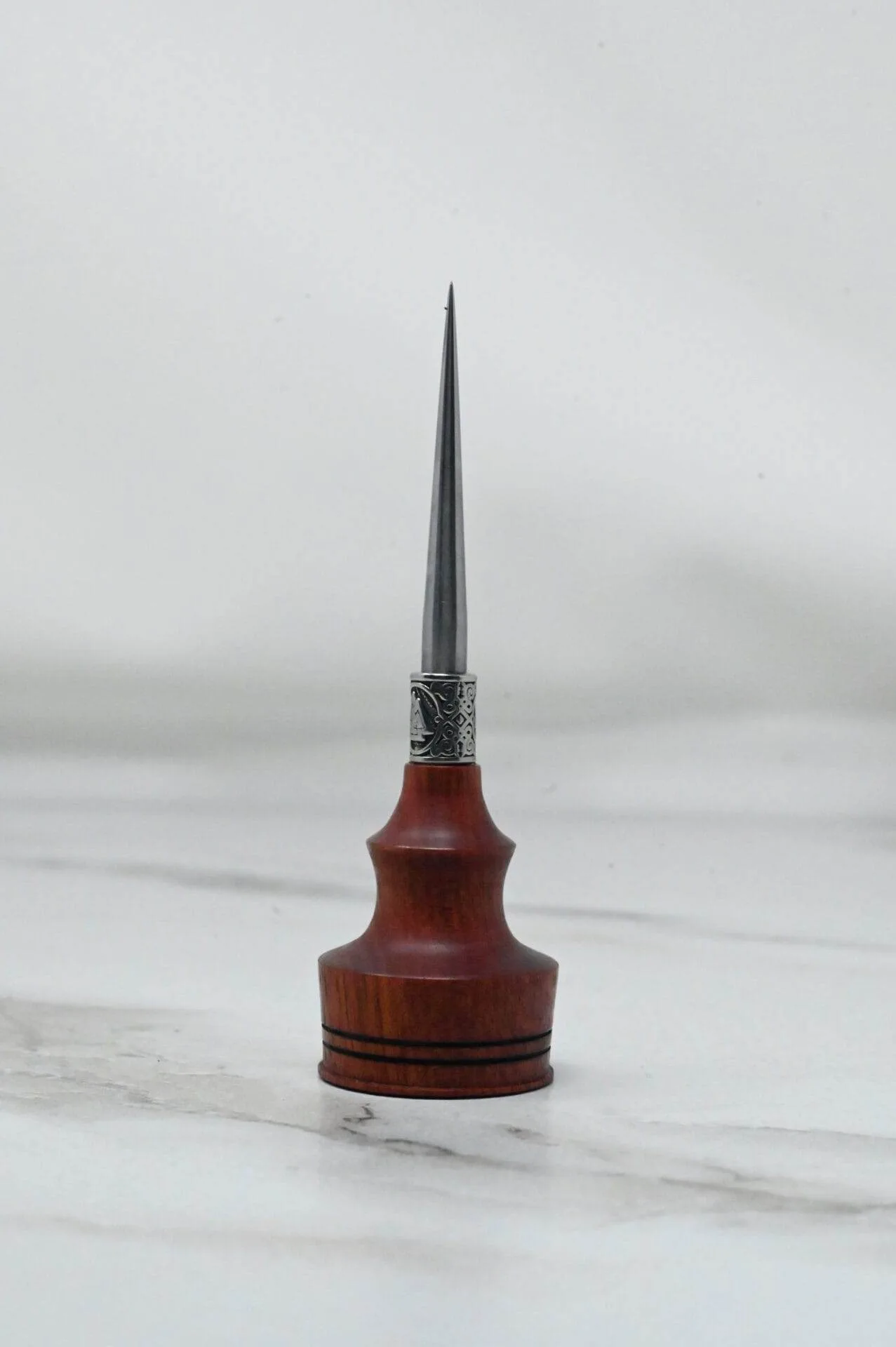 A small wooden Pre-release sale Japanese Leather Knife + Small Awl with a metal tip sitting on top of a marble table during the pre-release sale.