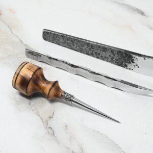 A 4th of July Leathercraft Bundle - 20 Sets Only! and a wood-handled awl with a pointed metal tip are laid out on a white marble surface.