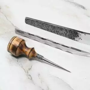 A 4th of July Leathercraft Bundle - 20 Sets Only! and a wood-handled awl with a pointed metal tip are laid out on a white marble surface.