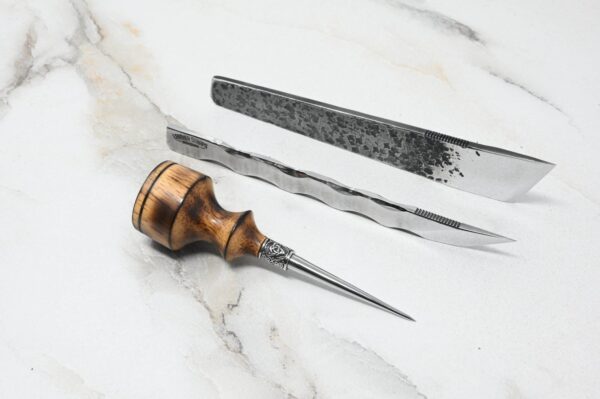 A 4th of July Leathercraft Bundle - 20 Sets Only! and a wood-handled awl with a pointed metal tip are laid out on a white marble surface.