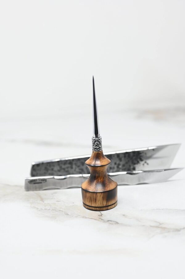 A small wooden-handled tool with a sharp, pointed metal tip from the 4th of July Leathercraft Bundle - 20 Sets Only! is placed in the foreground, with metallic tweezers in the background on a marble surface.