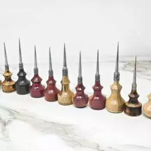 A row of eleven Premium Handmade to Order Scratch and Poking Awls with wooden handles in various shades, featuring metal tips, placed on a marble surface next to a ruler and a metal tool.