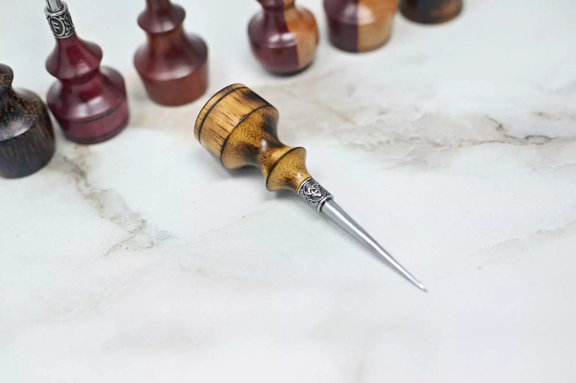 A handcrafted wooden handle awl with a metal tip is placed on a marble surface, surrounded by Premium Handmade to Order Scratch and Poking Awls and other Handmade Scratch Awls in the background.