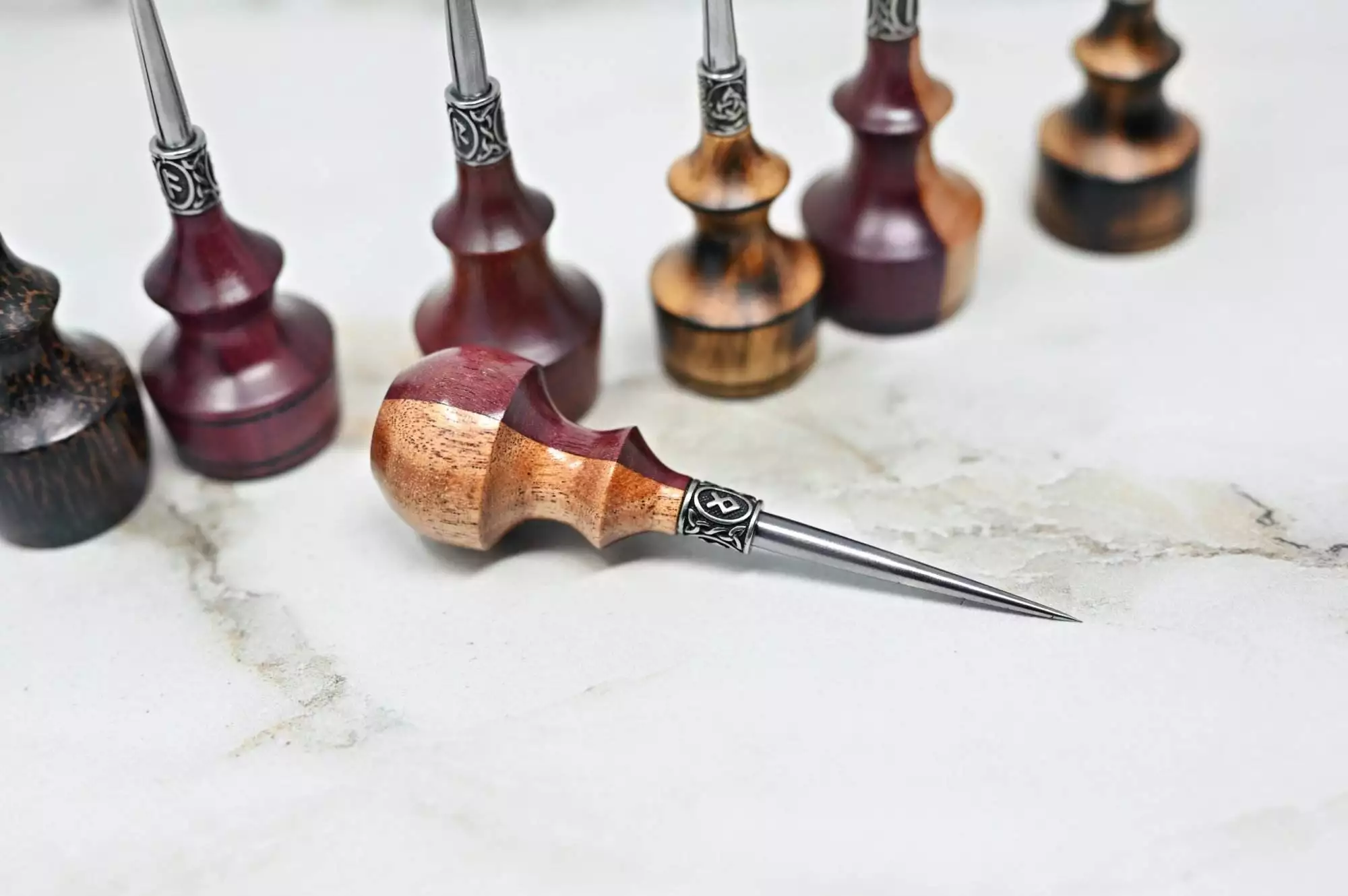 Several Premium Handmade to Order Scratch and Poking Awls are displayed on a marble surface, with one placed in the foreground.