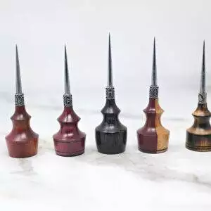 Five Premium Handmade to Order Scratch and Poking Awls with wood handles and metal tips stand upright on a white marble surface, each featuring different shades and grain patterns of wood.