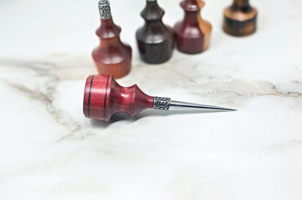 A Premium Handmade to Order Scratch and Poking Awls lies on a marble surface, surrounded by other similar tools, including scratch awls and poking awls.