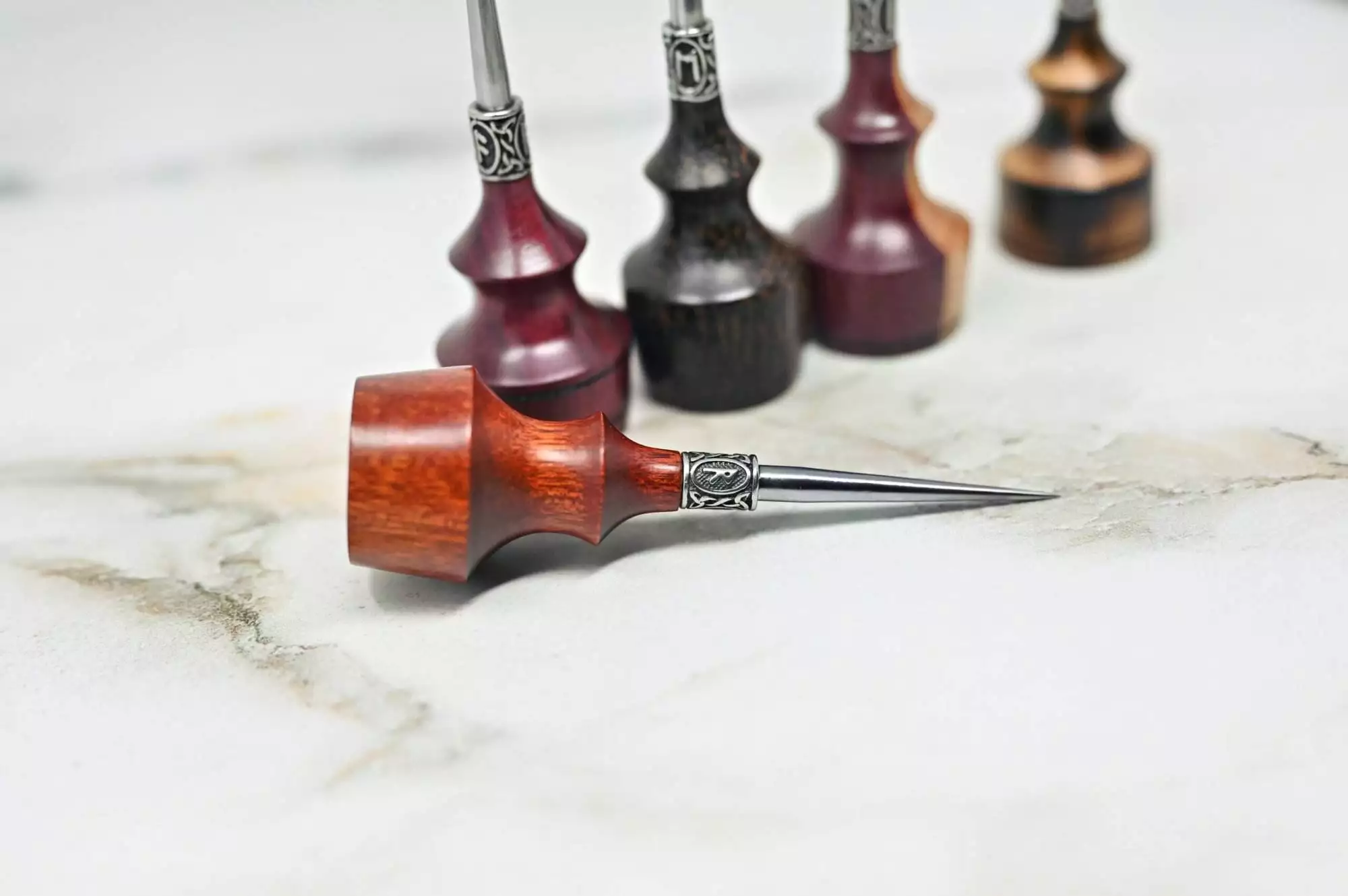 A set of Premium Handmade to Order Scratch and Poking Awls, featuring various shades of wood, positioned upright on a white marble surface, with one poking awl lying horizontally in the foreground.