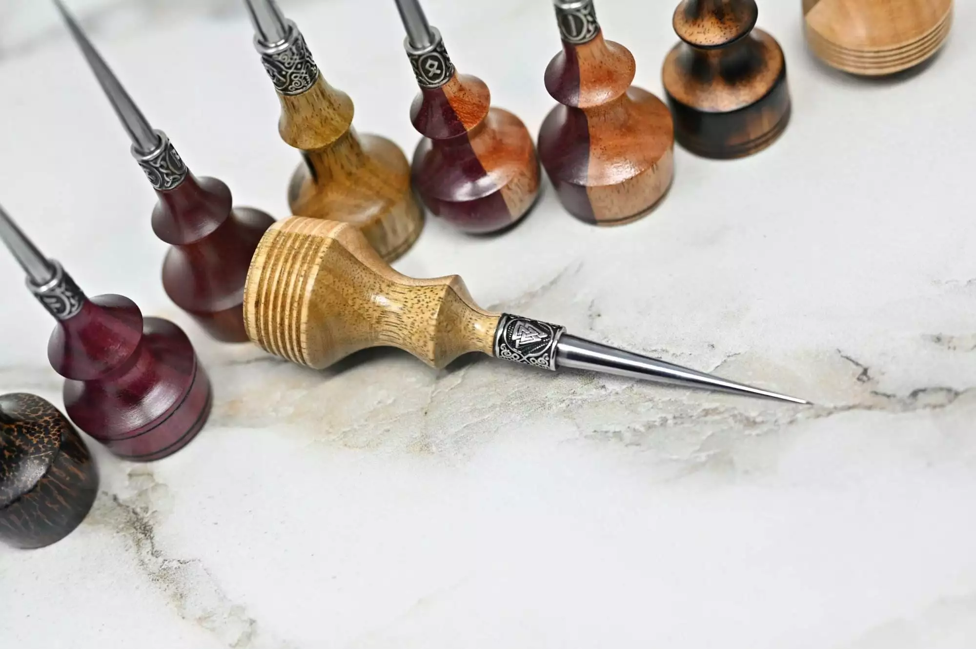 A collection of Premium Handmade to Order Scratch and Poking Awls with wooden handles arranged on a marble surface, featuring one uniquely positioned in the foreground.