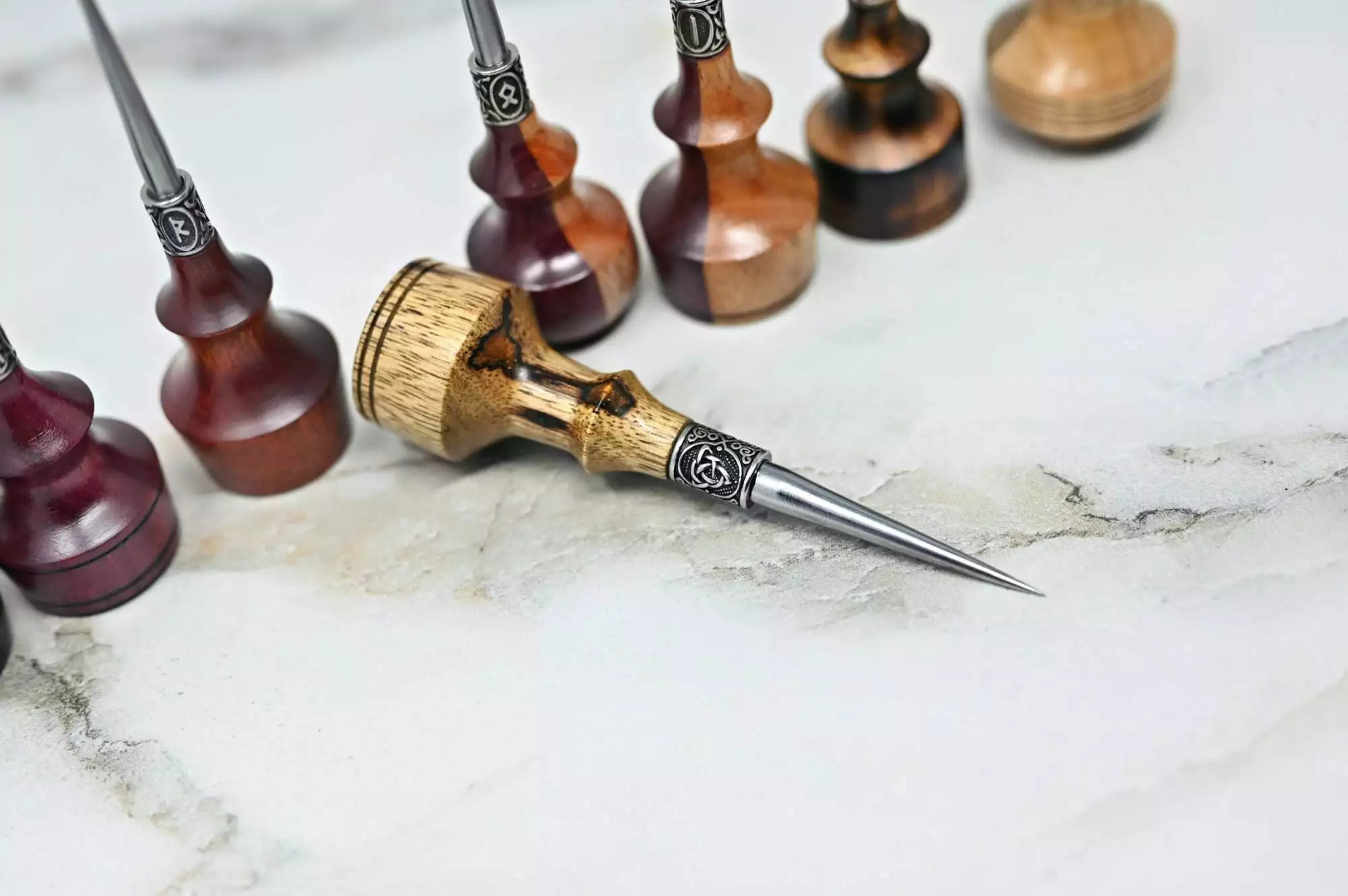 Close-up of several handmade scratch awls displayed on a marble surface. One Premium Handmade to Order Scratch and Poking Awl is laid horizontally in the foreground.