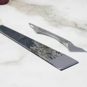 Two straight razors are laid out on a marble surface: a rectangular Fang with a worn blade and an Essential Skiver, smoother modern one with a distinct curve.