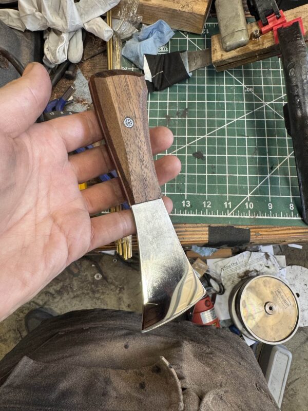 A person holds the "Signature" Leather Knife accompanied by a handmade awl. The background features a cutting mat and various tools.