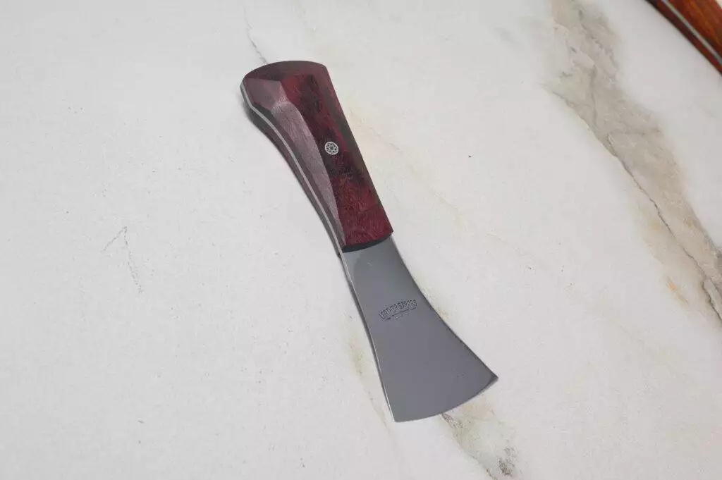 A compact Leather Knife from the "Signature" collection with a wooden handle and gray blade resting on a marble surface.