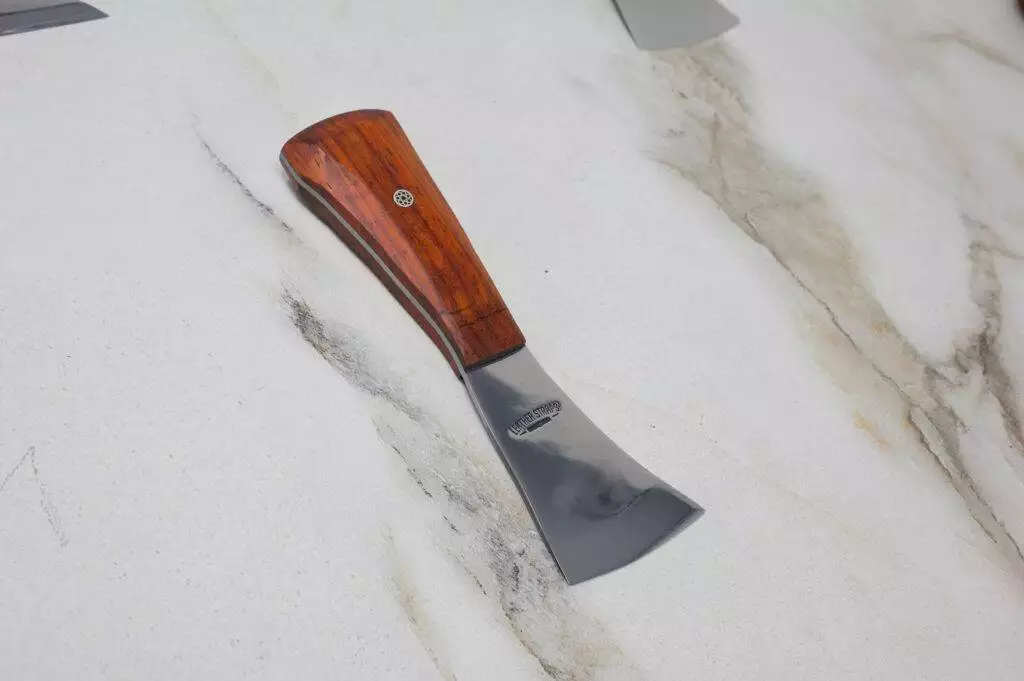 The "Signature" Leather Knife with a wide metal blade rests on a marbled surface.