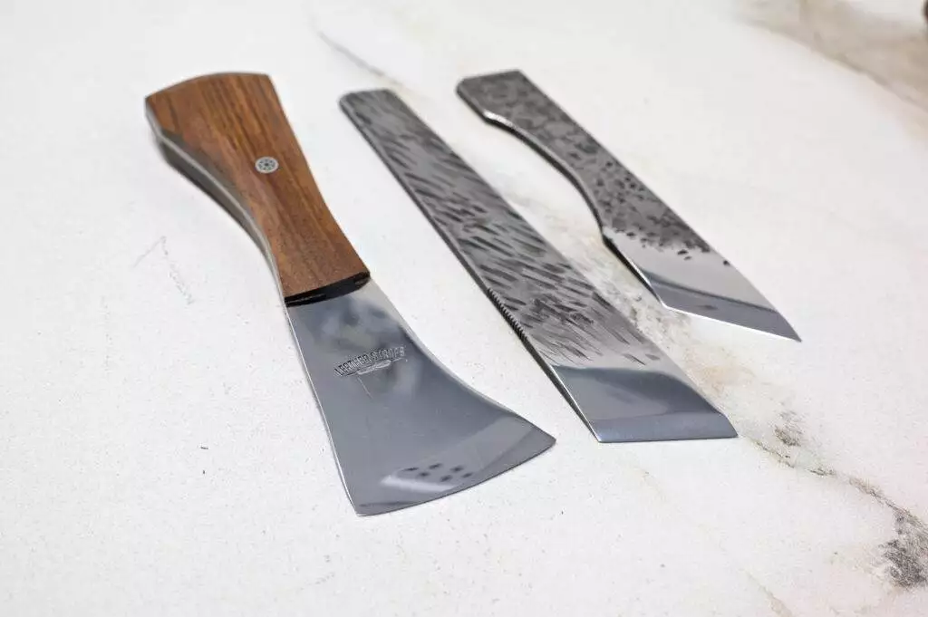 The Halloween 3 Piece Special, a set of Japanese wood carving knives with polished blades and distinct wooden handles, is elegantly arranged on a marble surface.