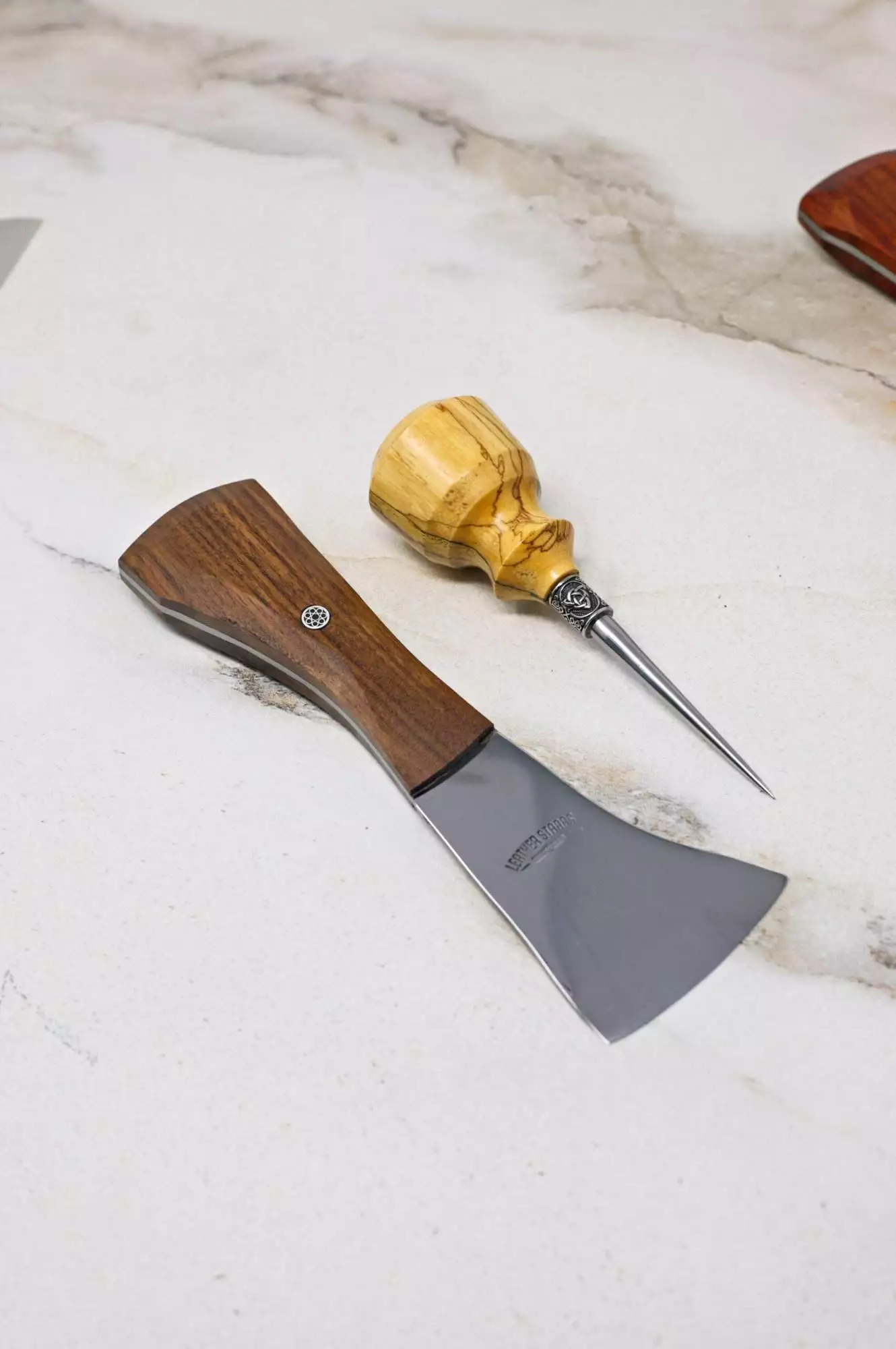 A small axe featuring a wooden handle and a woodworking awl rest on the white marble surface, completing The Halloween 3 Piece Special arrangement.