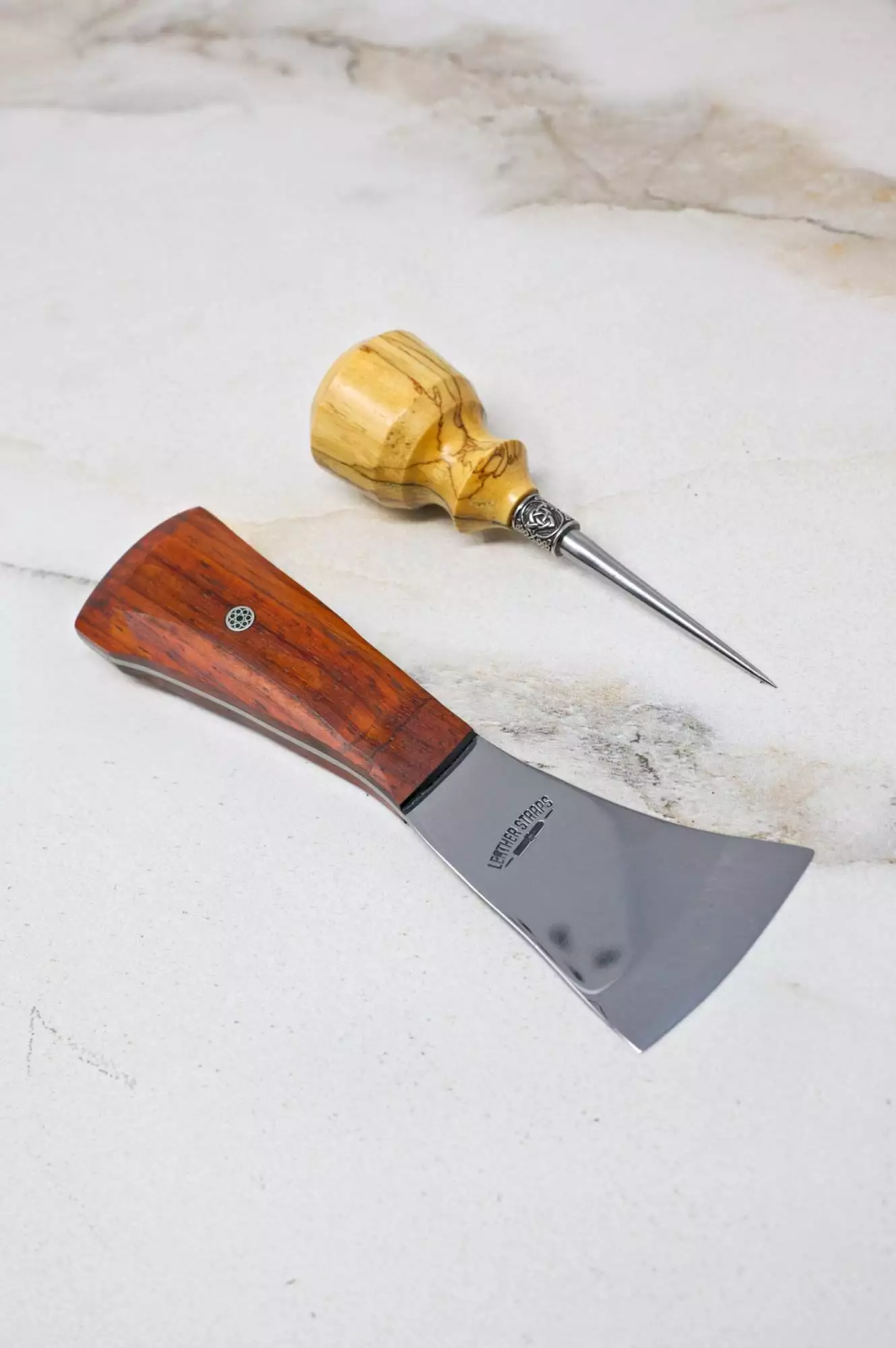 A woodworking chisel featuring a wooden handle and a polished metal blade rests next to a wooden-handled awl on a light-colored surface, perfectly suited to enhance your Halloween projects or complete your collection of The Halloween 3 Piece Special.