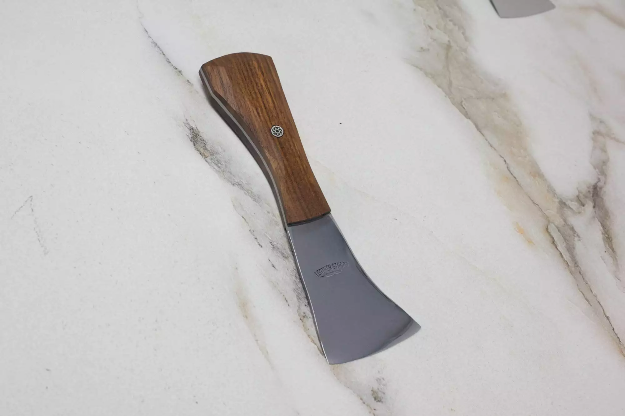 The "Signature" Leather Knife with its wooden handle and metal blade is resting on a light-colored marbled surface.