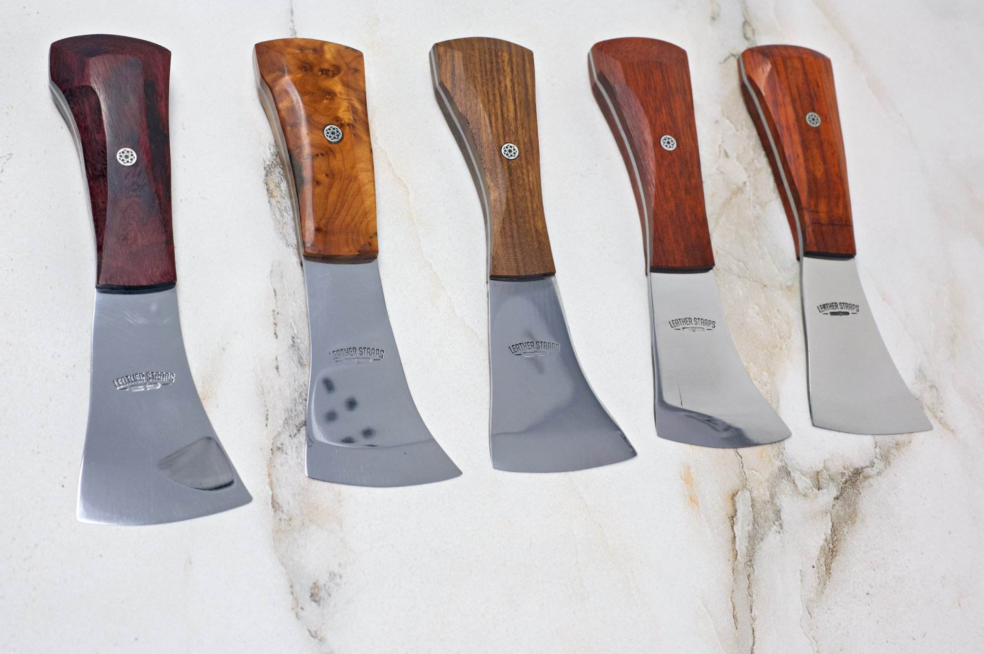 Five cheese knives with wood handles and stainless steel blades are lined up in a row on a marble surface, making them ideal for your Halloween gathering or as part of The Halloween 3 Piece Special.