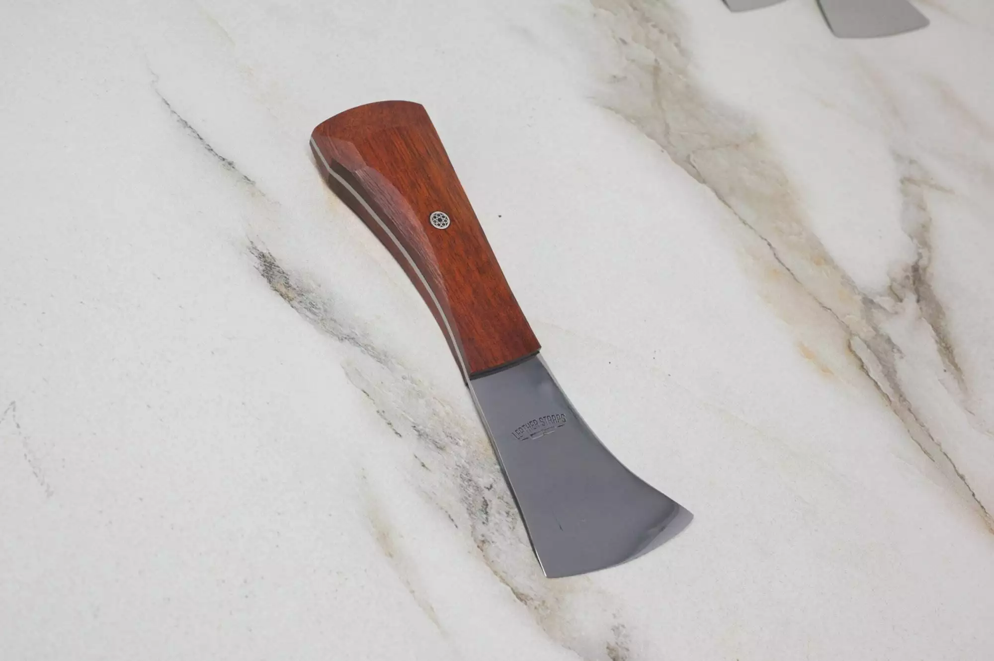 The "Signature" Leather Knife, featuring a compact design with a wooden handle and a silver blade, lies on a marble surface.