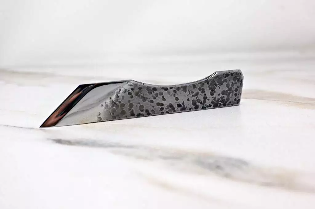 A sleek, patterned knife from The Halloween 3 Piece Special, boasting a sharp blade, rests ominously on a marble surface—ideal for your Halloween preparations.