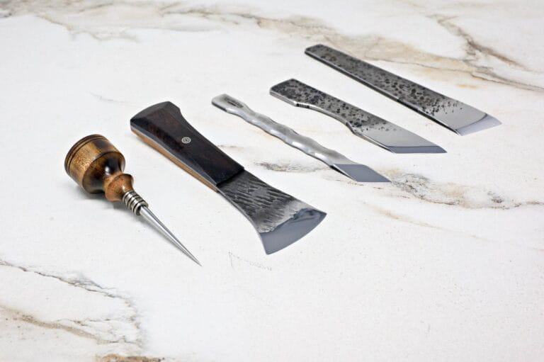 A collection of four "Signature" Leather Knives featuring wooden and metal handles, elegantly arranged on a light stone surface.