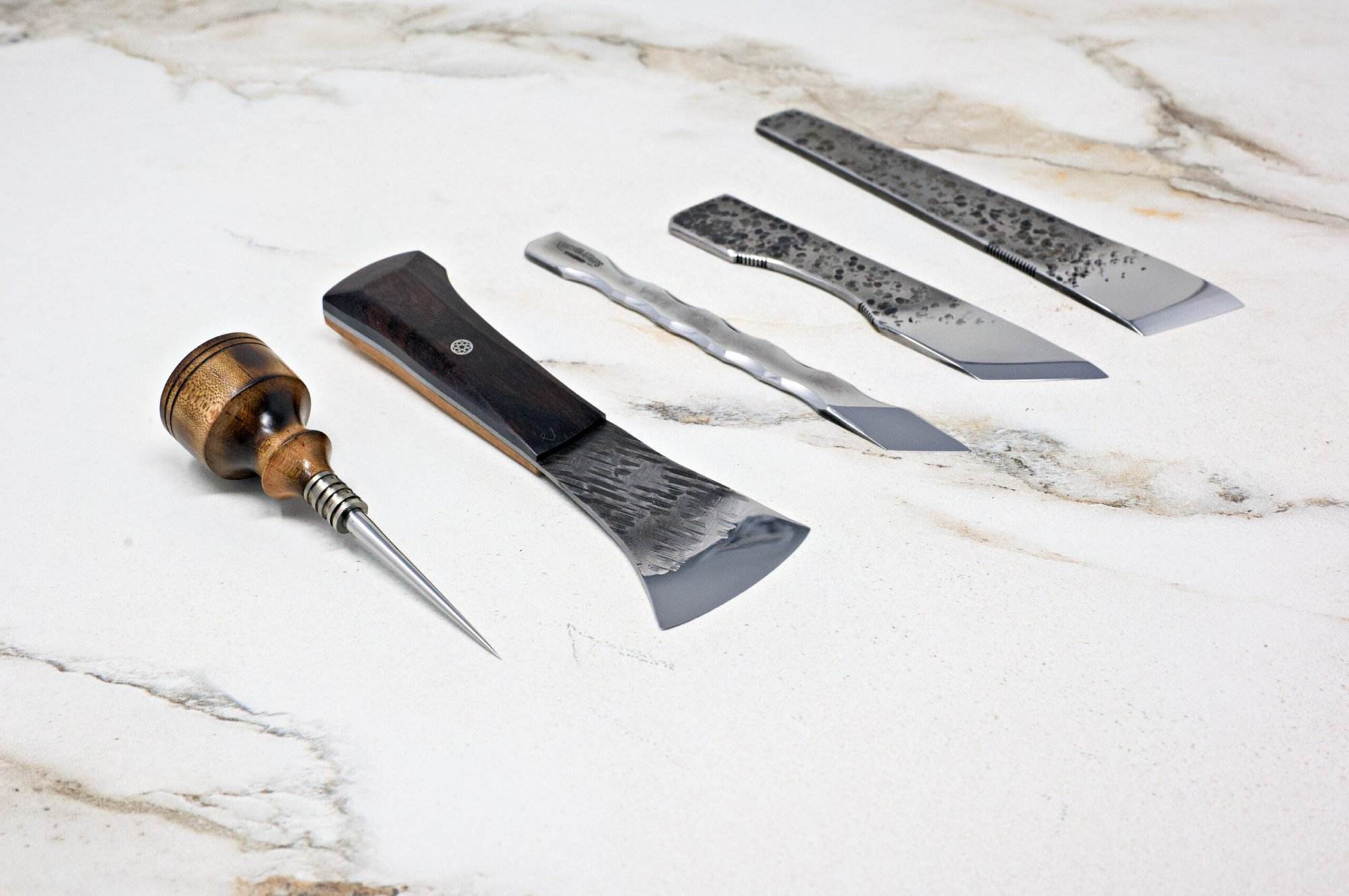 A collection of four "Signature" Leather Knives featuring wooden and metal handles, elegantly arranged on a light stone surface.