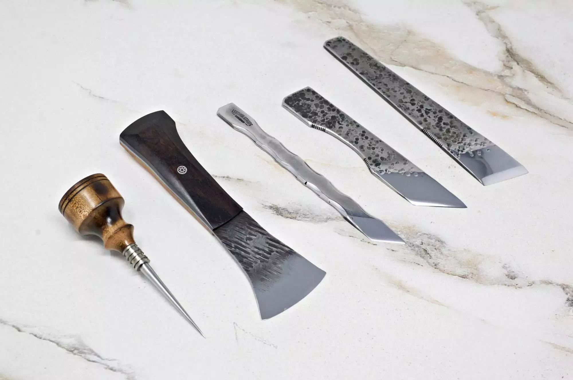 A set of five "Signature" Leather Knives, expertly crafted from metal and wood, displayed on a light marble surface.