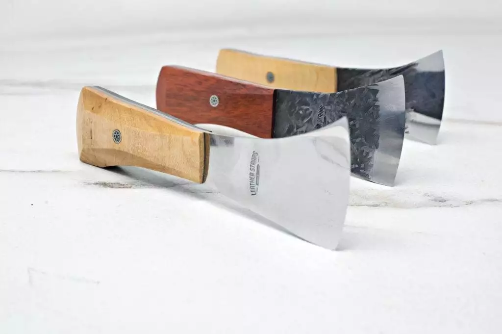 Three "Signature" Leather Knives with shiny blades and wooden handles are arranged in a staggered line on a white surface.