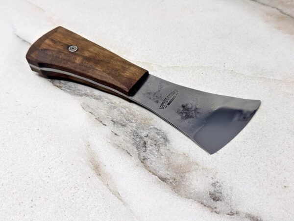 The "Charlie" Leather Knife, featuring a small axe with a wooden handle and sharp metal blade, rests on the marble surface alongside its handmade awl.