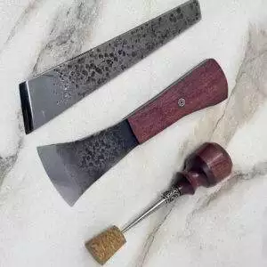 A forged custom three-piece metal and wood carving tool set for left-handed users, featuring a cork with a decorative pin, elegantly rests on the marble surface.