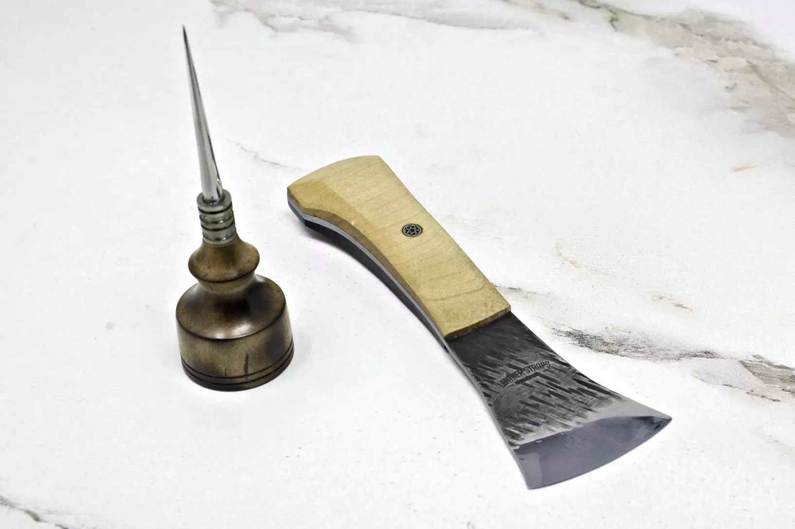 The "Signature" Leather Knife and Handmade Awl, both crafted with elegant wooden handles, rest gracefully on a white marble surface.