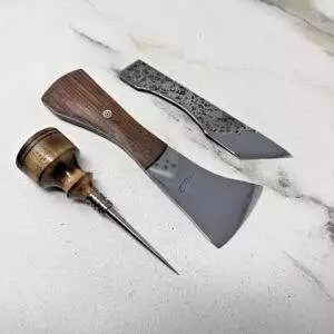 A set of wood carving tools on a white surface features the Black Walnut Signature Knife, a Scorpion Skiver, and a Burnt Ambrosia Maple Awl.