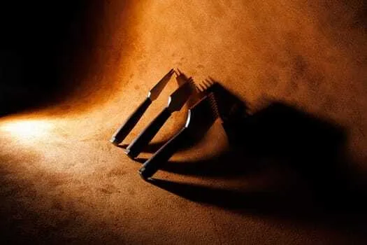 Three leathercraft tools with pronged ends are arranged on a brown suede surface, casting shadows under warm lighting, perfect for creating clean corner cuts.
