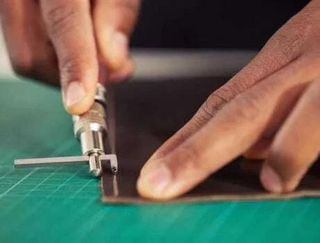 Close-up of hands expertly crafting clean corner cuts with a precision knife on a green cutting mat, perfecting the art of leathercraft.