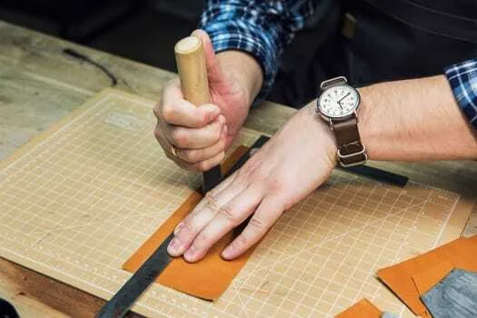 A person expertly uses a chisel to achieve clean corner cuts on a piece of leather laid out on the cutting mat. A ruler is carefully placed for precision, showcasing the art of leathercraft.