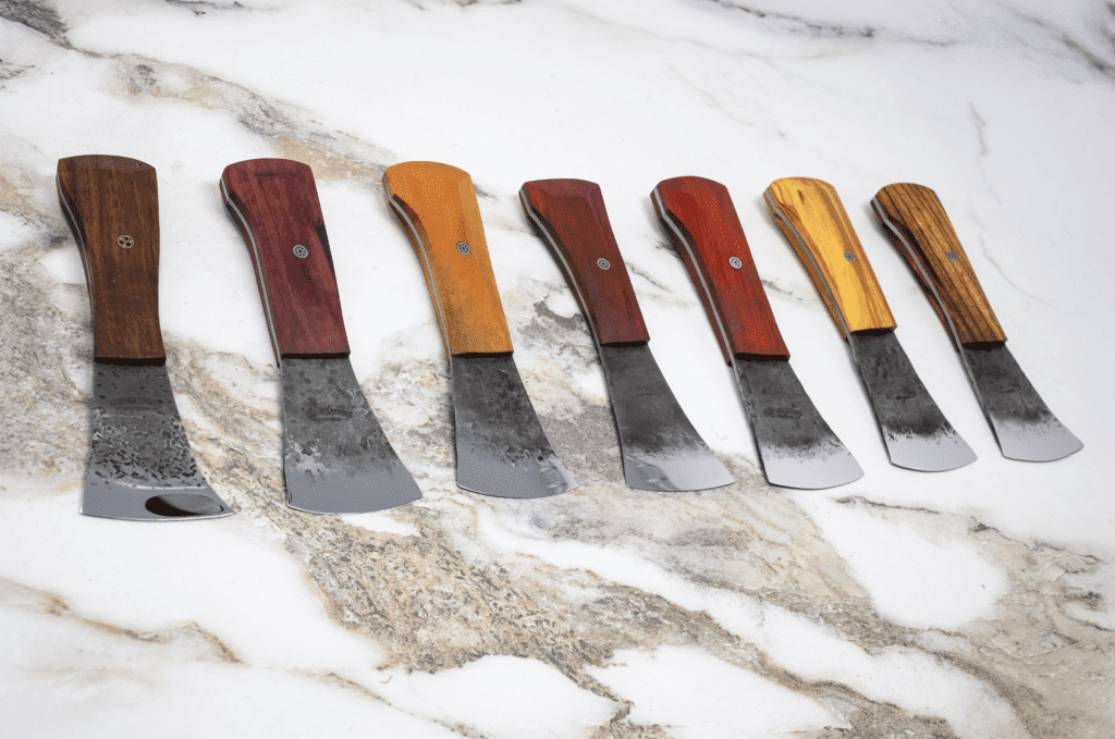 The 2025 Valentines Day - The Essentials Special features seven cleavers with wooden handles in various colors, beautifully arranged on marble—perfect for enhancing your culinary collection.