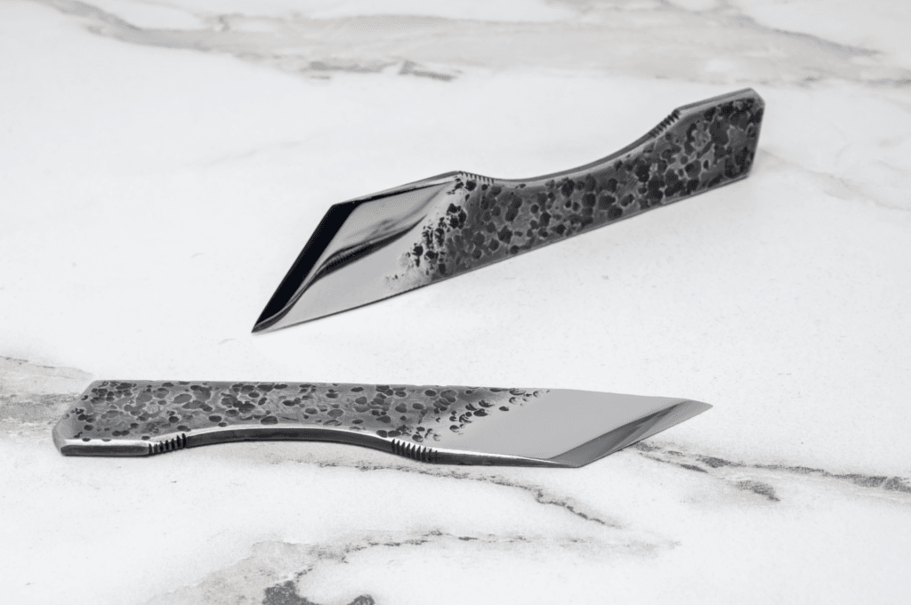 Two sleek stainless steel knives with textured, speckled handles elegantly rest on a white marble surface, making them an ideal fit for any culinary adventure. Discover them in the 2025 Valentines Day - The Essentials Special.