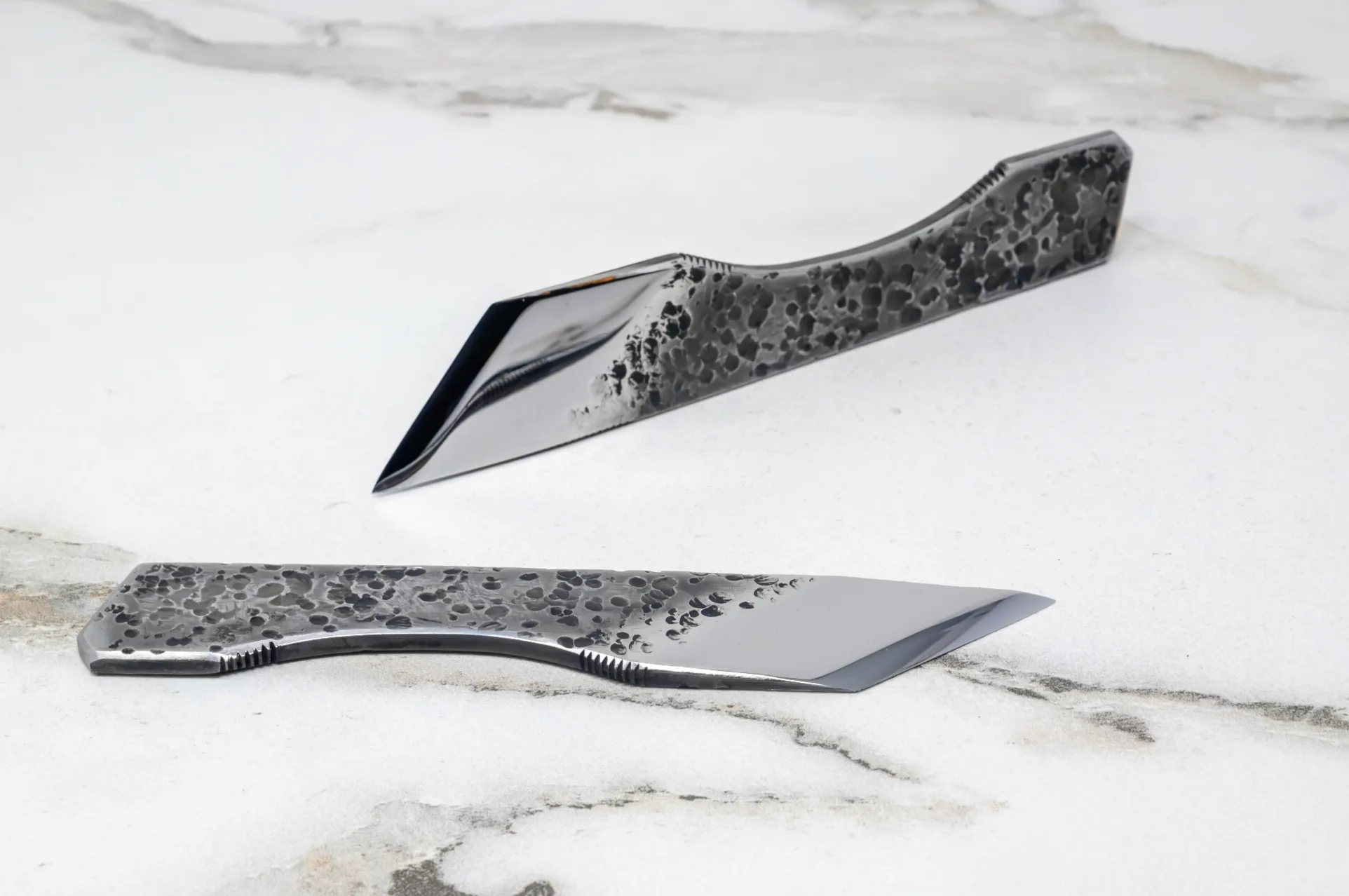 Two sleek stainless steel knives with textured, speckled handles elegantly rest on a white marble surface, making them an ideal fit for any culinary adventure. Discover them in the 2025 Valentines Day - The Essentials Special.