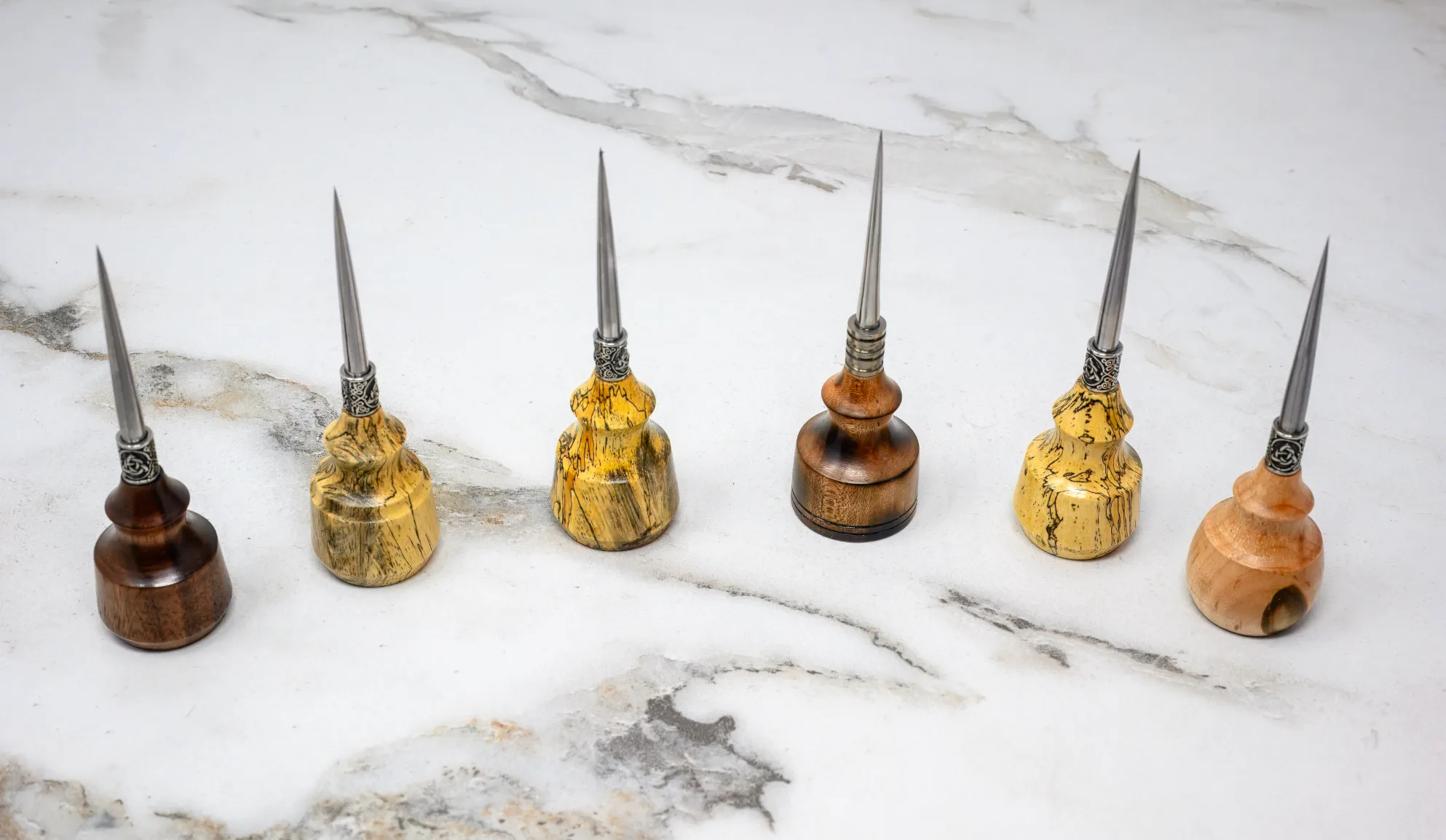 Six handcrafted awls with wooden handles and pointed metal tips are lined up on a light marble surface, highlighting the 2025 Valentines Day - The Essentials Special for every artisan's toolbox.