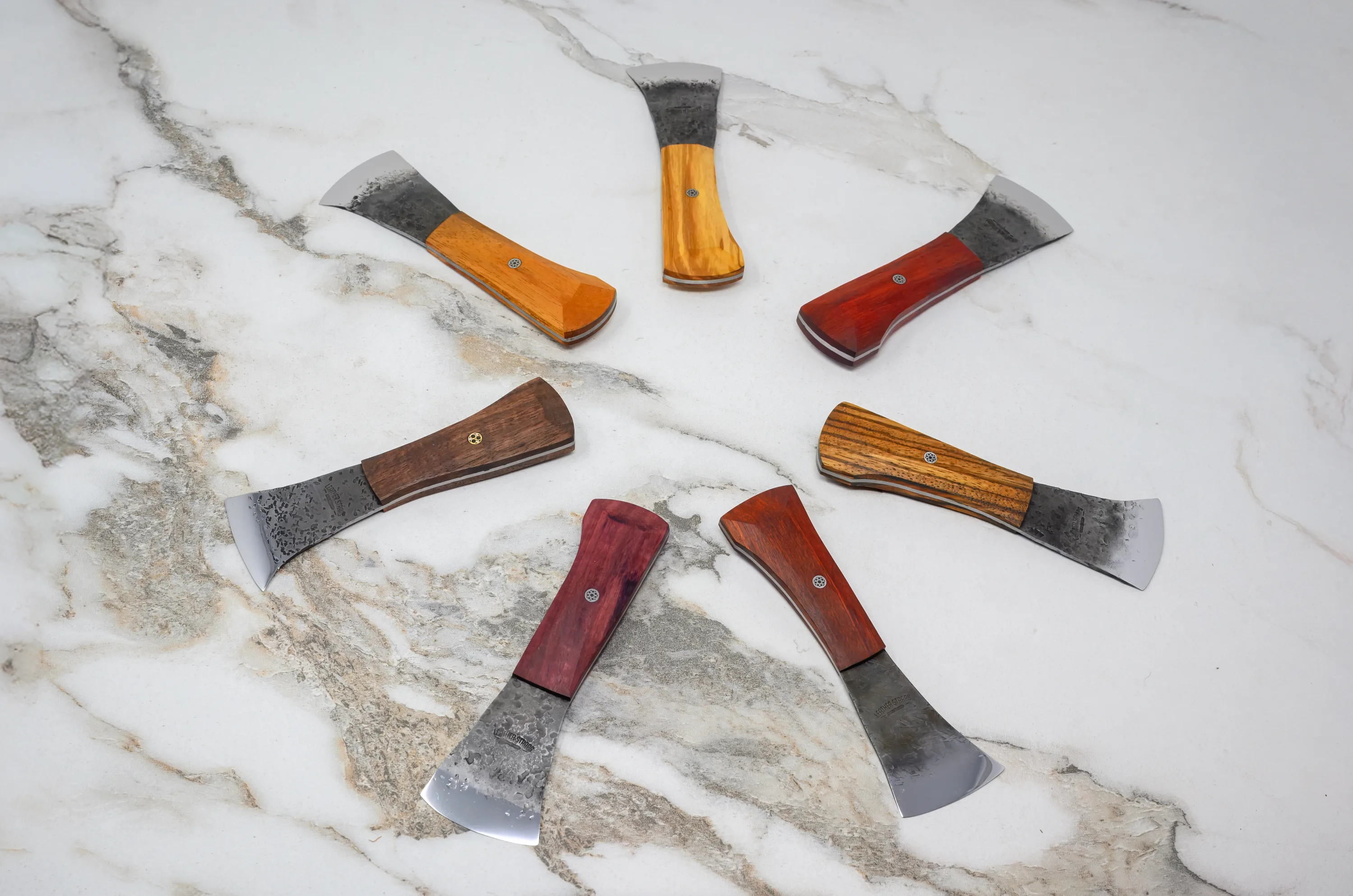 The 2025 Valentine's Day - The Essentials Special features a circular arrangement of seven small axes, each with distinct wooden handles, displayed on a marbled surface.