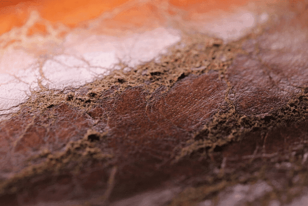 Close-up of brown leather texture showcasing the artistry of leathercraft with visible wear and cracks, highlighting the beauty of patina development.