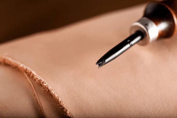 Close-up of a leather crafting tool resting on a piece of tan full grain leather fabric with frayed edges.